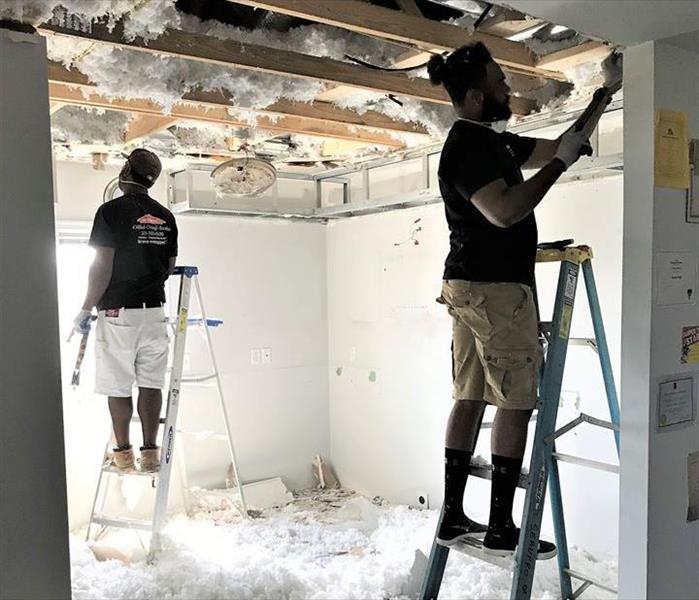 2 Servpro employees standing on stools and ripping out a damaged ceiling